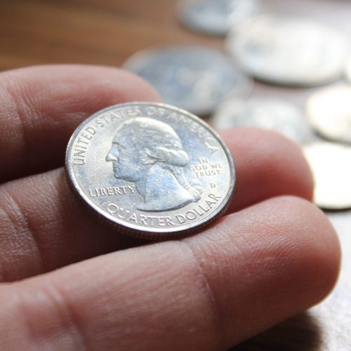 hand picking up a quarter coin in american currency spread on the wooden floor